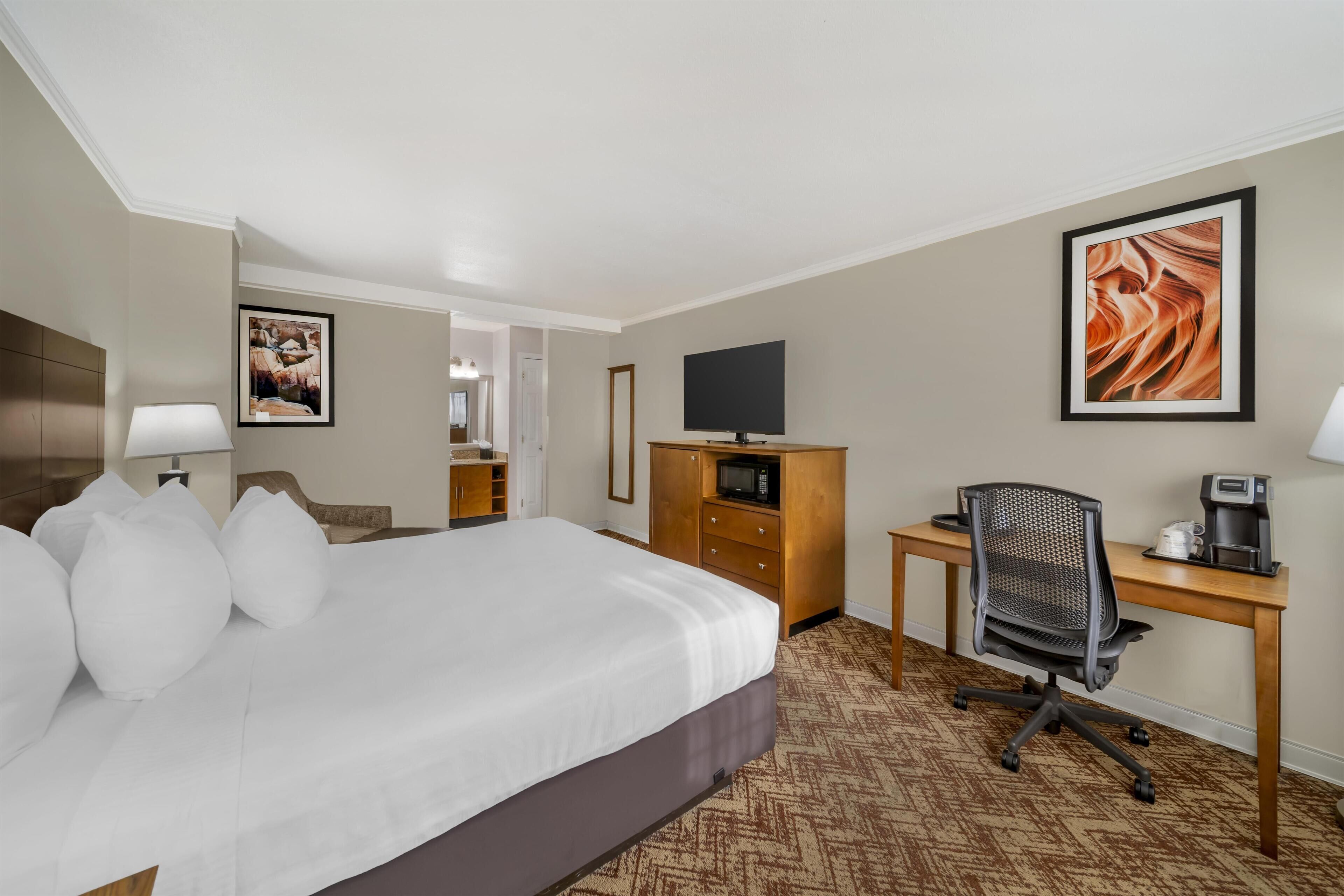 A hotel room with a large bed, a desk with a chair, a television, and a microwave.