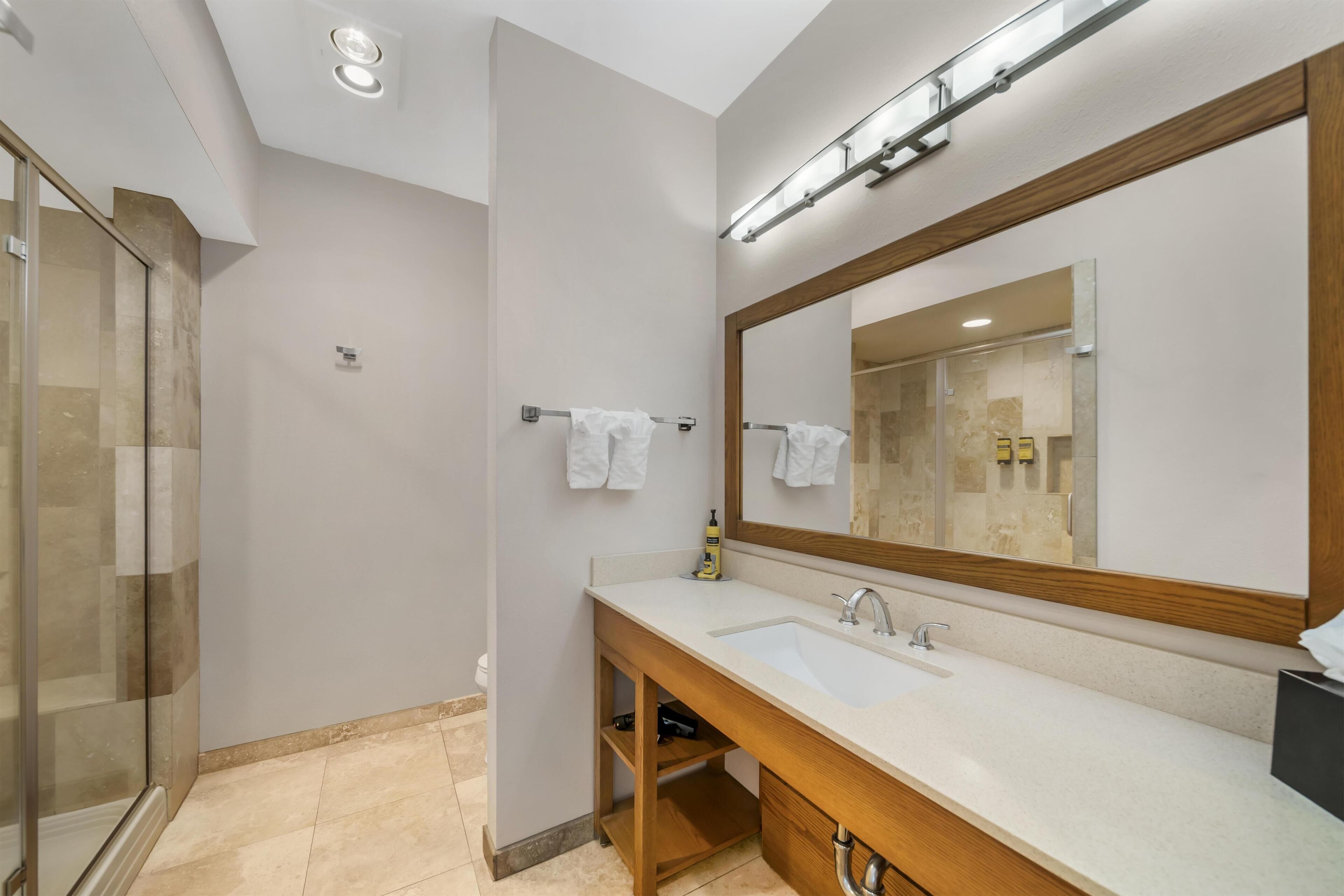 A modern bathroom with a large mirror, two sinks, and a glass shower enclosure.