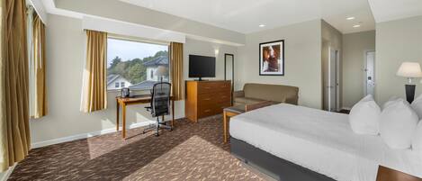 A hotel room with a large bed, a desk with a chair, a dresser, a TV, and a window with curtains.