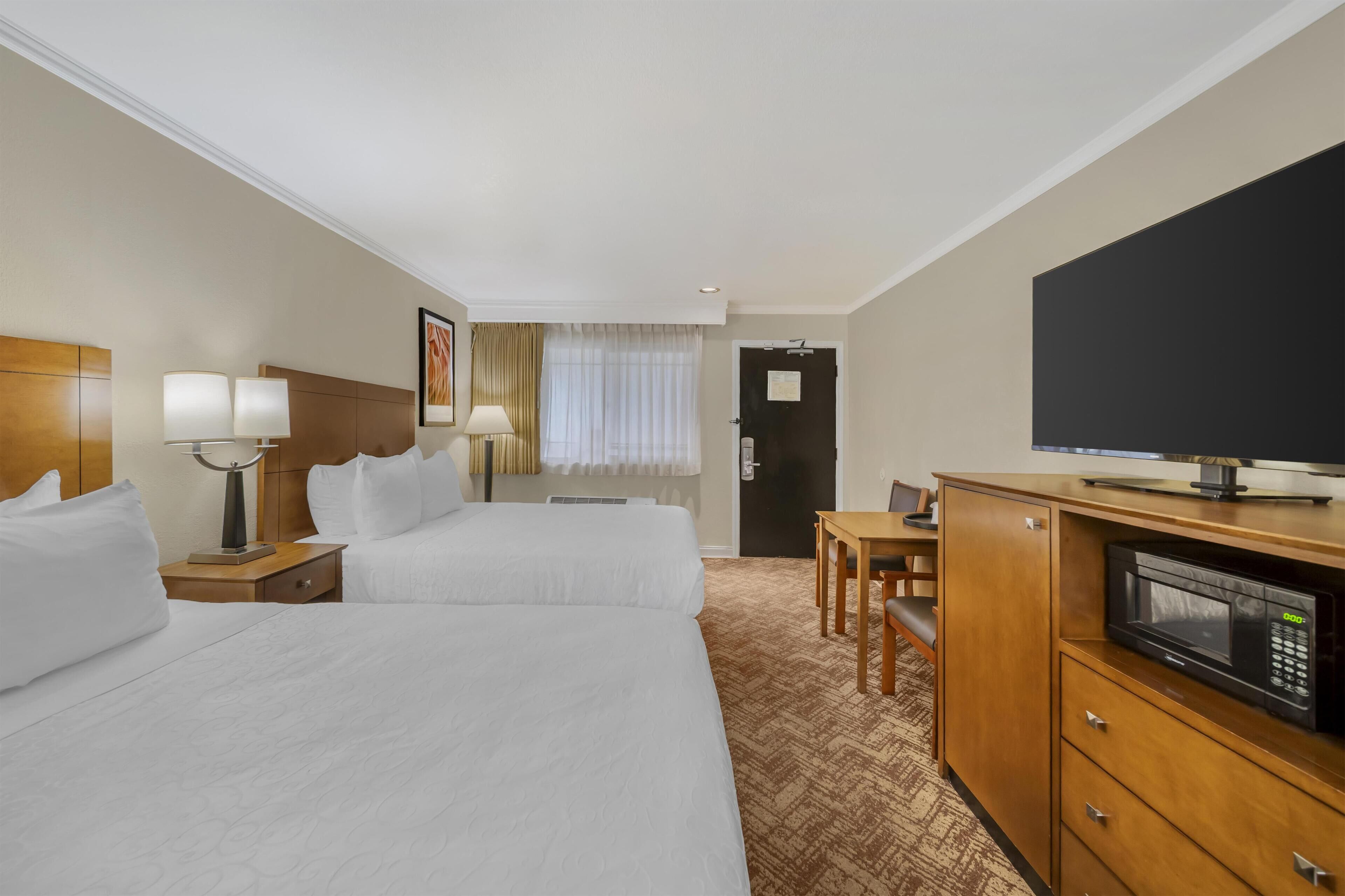 Quarto de hotel com duas camas, uma escrivaninha, televisão e micro-ondas.