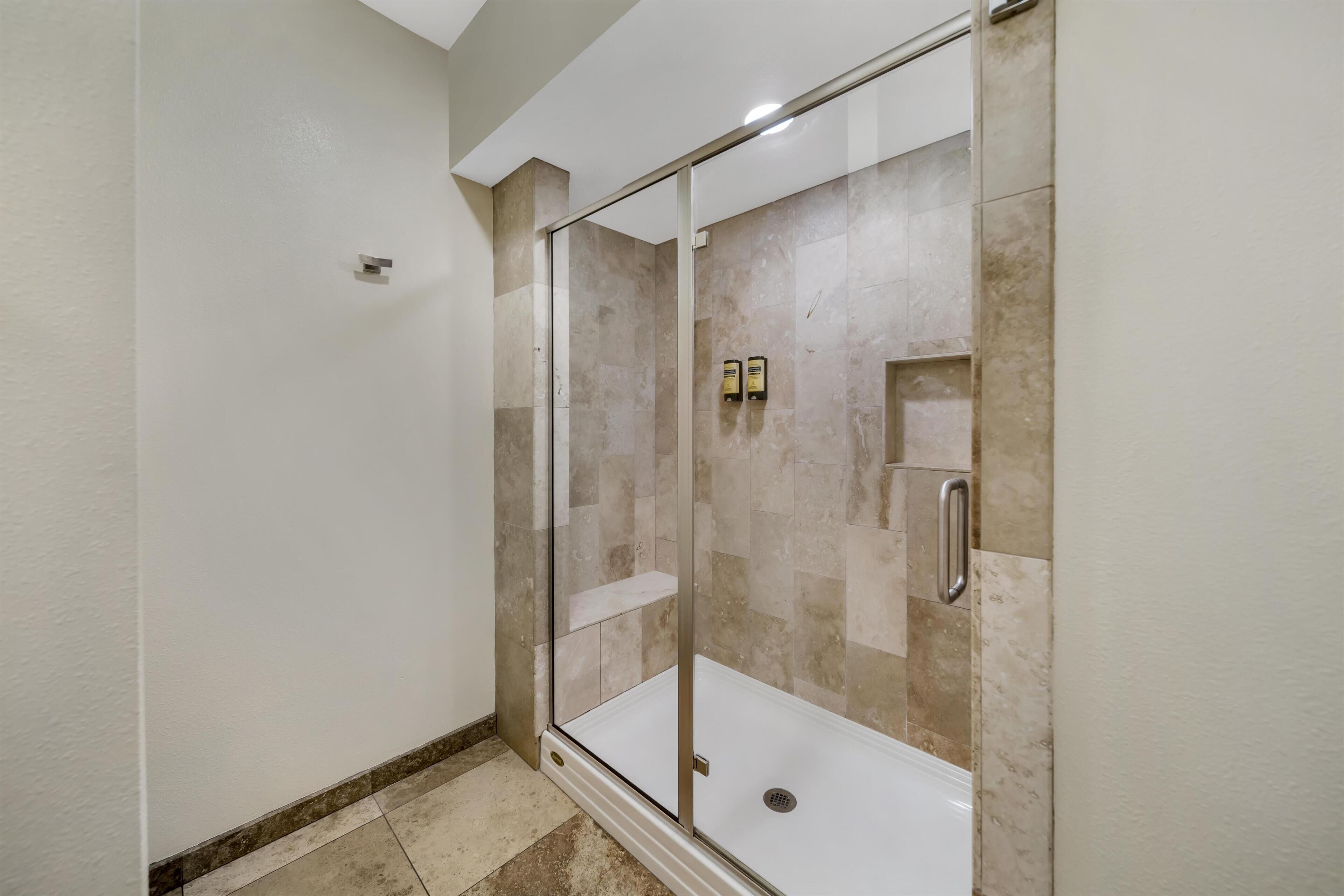A modern bathroom with a glass-enclosed shower, beige tiles, and a white bathtub.