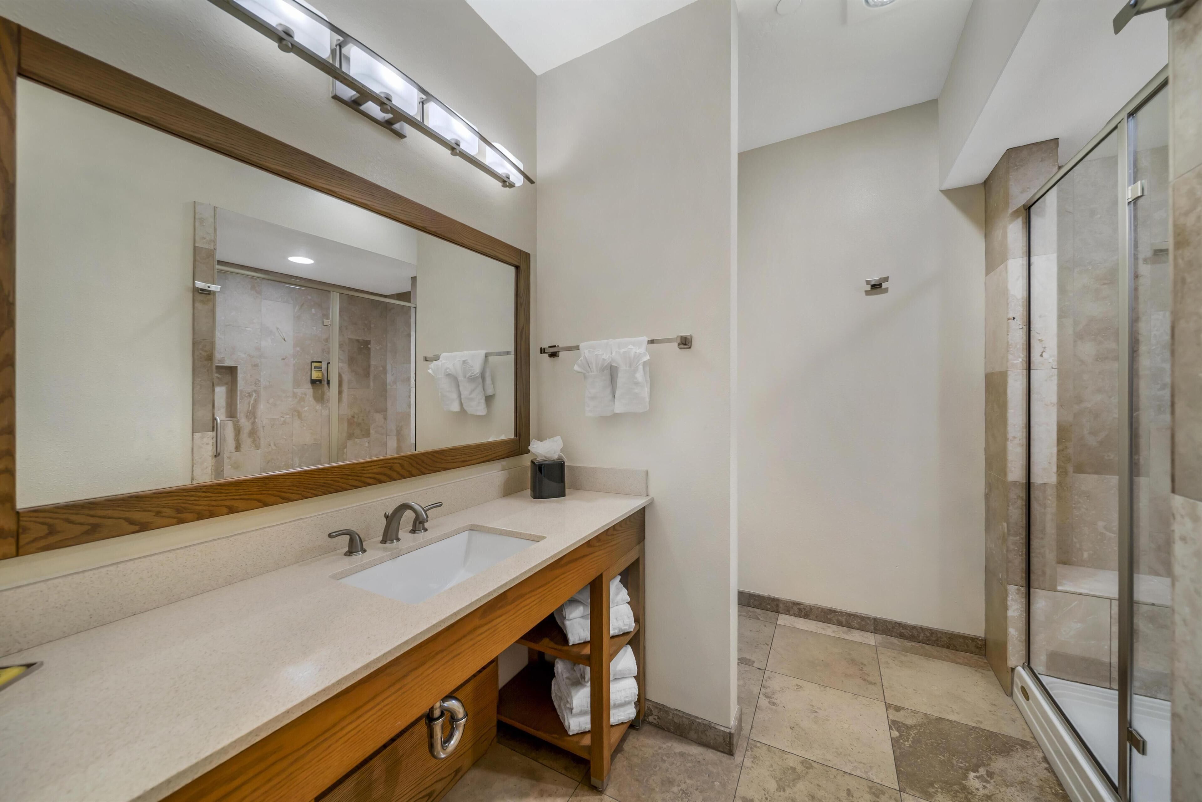 A bathroom with a wooden vanity, a large mirror, a sink, and a glass shower enclosure.
