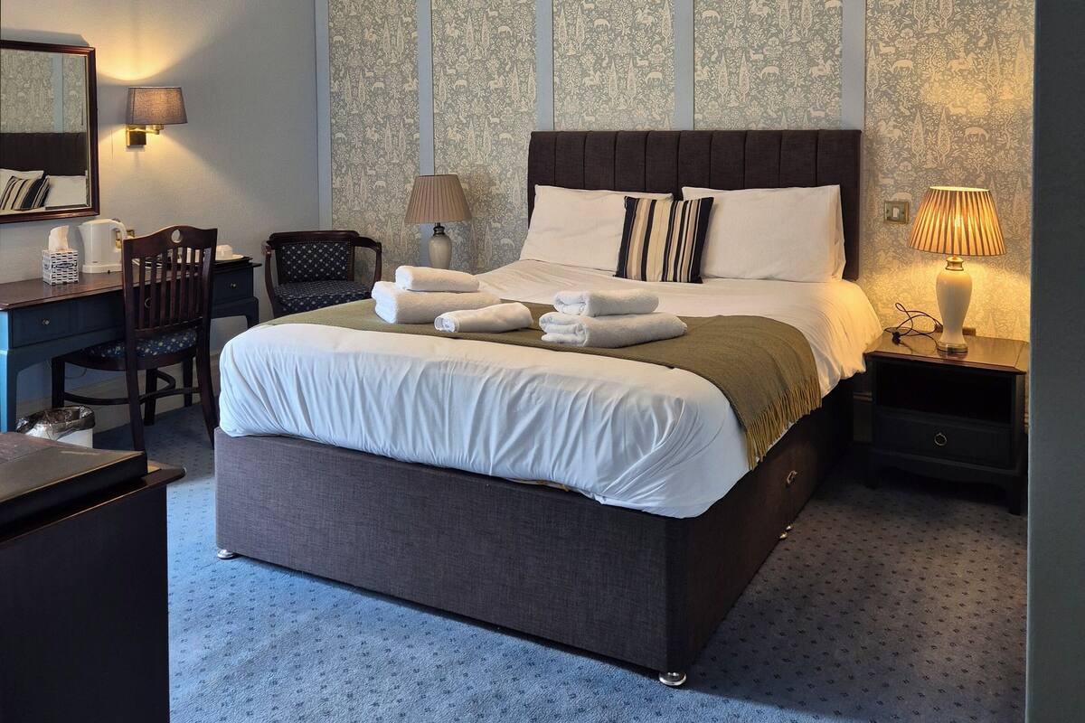 A neatly arranged hotel room with a large bed, a desk, a chair, and a nightstand.