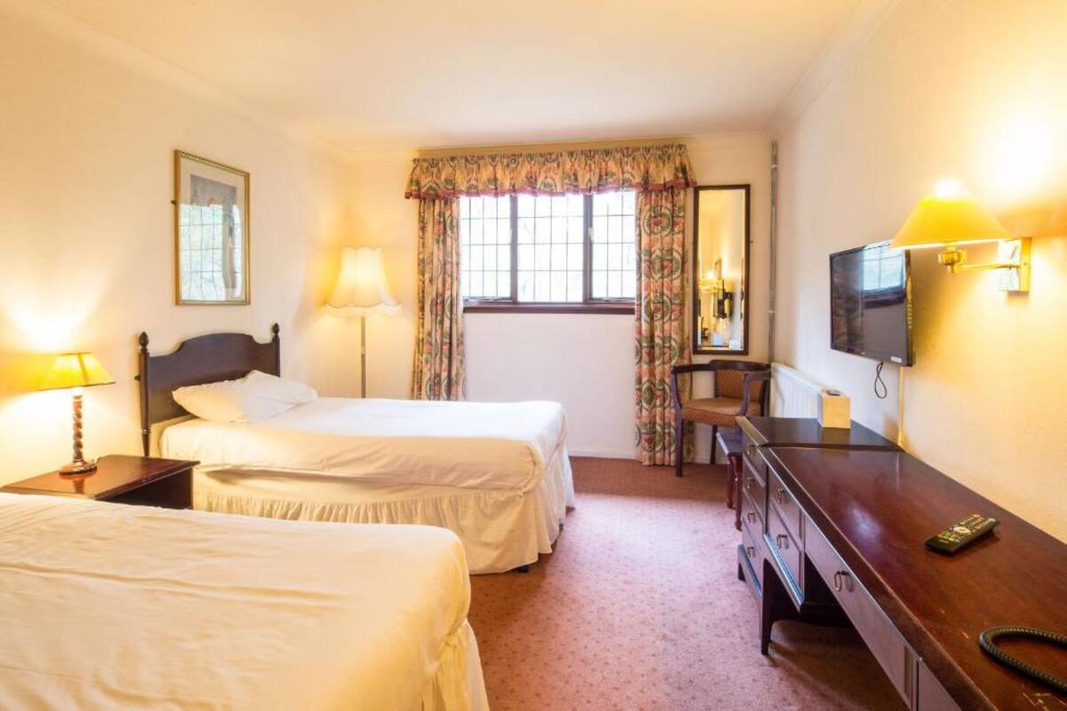 A hotel room with two beds, a desk, a chair, a TV, and a mirror.