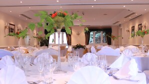 Une salle de banquet avec des tables rondes dressées pour un événement formel, agrémentées de nappes blanches, de verres et de compositions florales.