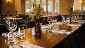 Une table de restaurant dressée avec des verres à vin, un vase rempli de fleurs et des couverts soigneusement disposés.