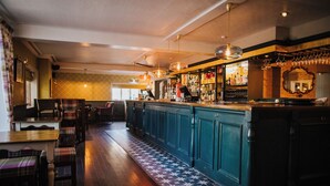 Un espace bar doté d’un plancher en bois, d’un revêtement de sol à motifs devant le bar, et d’un comptoir où sont exposées diverses bouteilles et verres.