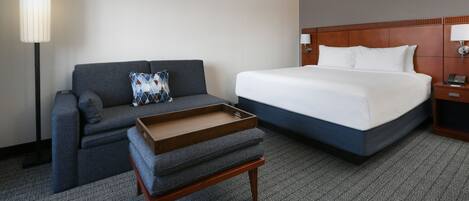 Quarto de hotel com cama, sofá, uma mesinha e um abajur.
