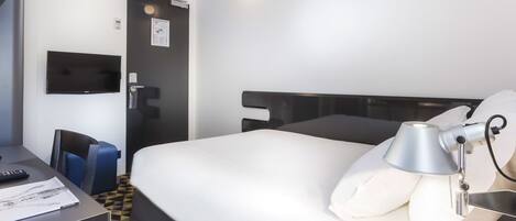 Une chambre d’hôtel avec un lit, un bureau, une chaise, une télévision et une lampe.