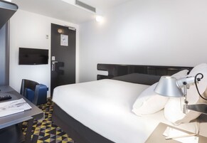 A hotel room with a bed, a desk, a chair, a TV, and a lamp.