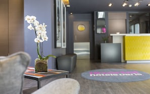 Un espace d’accueil comprenant un comptoir de réception, une plante à fleurs blanches et un tapis rond orné de motifs.