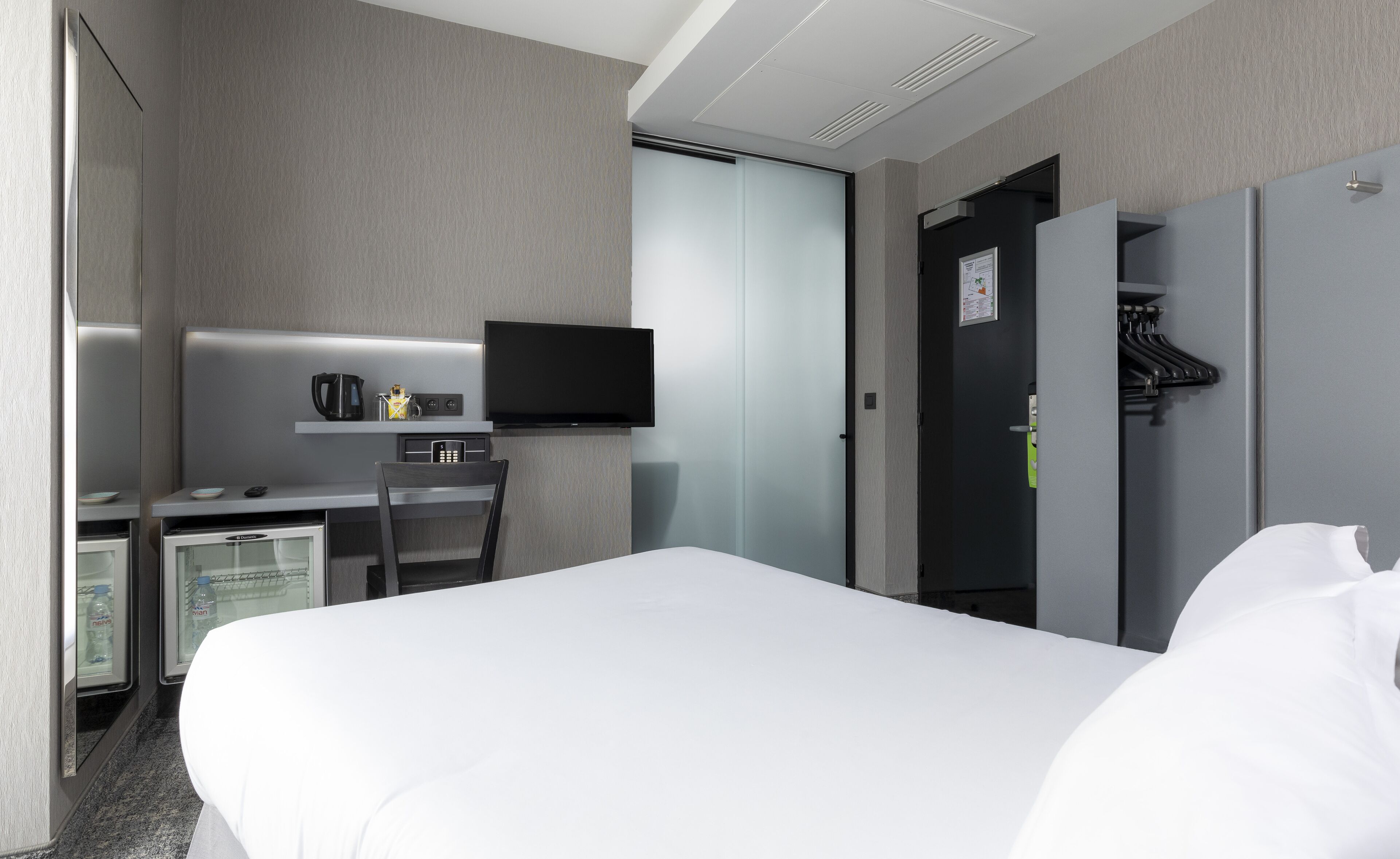 A hotel room with a bed, a desk with a television, a coffee maker, and a wardrobe.