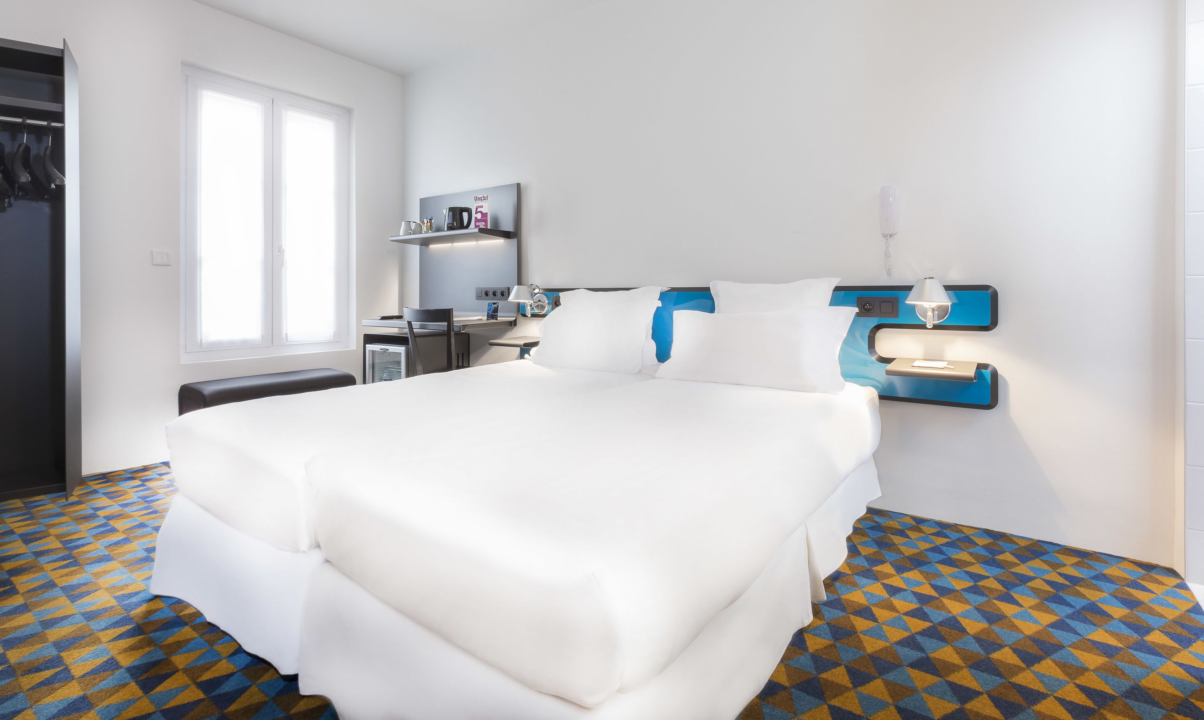 A hotel room with a bed, a desk, a chair, a wardrobe, and a window.