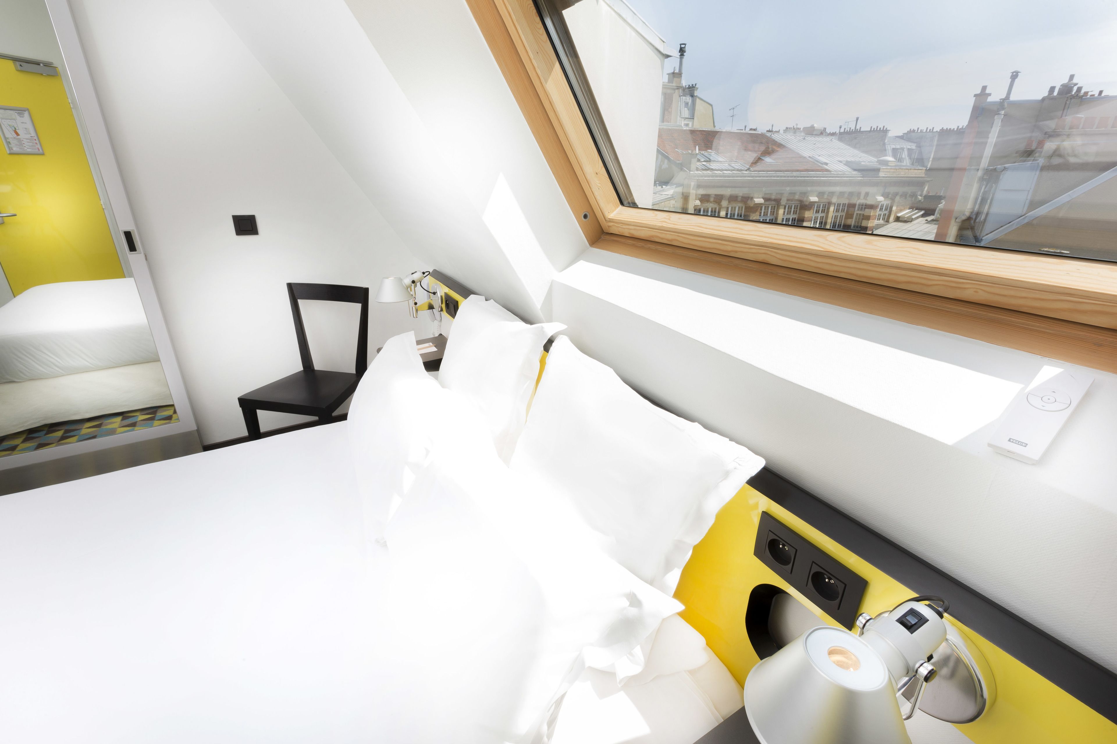 A hotel room with a bed, a chair, a desk, and a window with a view of buildings.