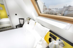 A hotel room with a bed, a chair, a desk, and a window with a view of buildings.