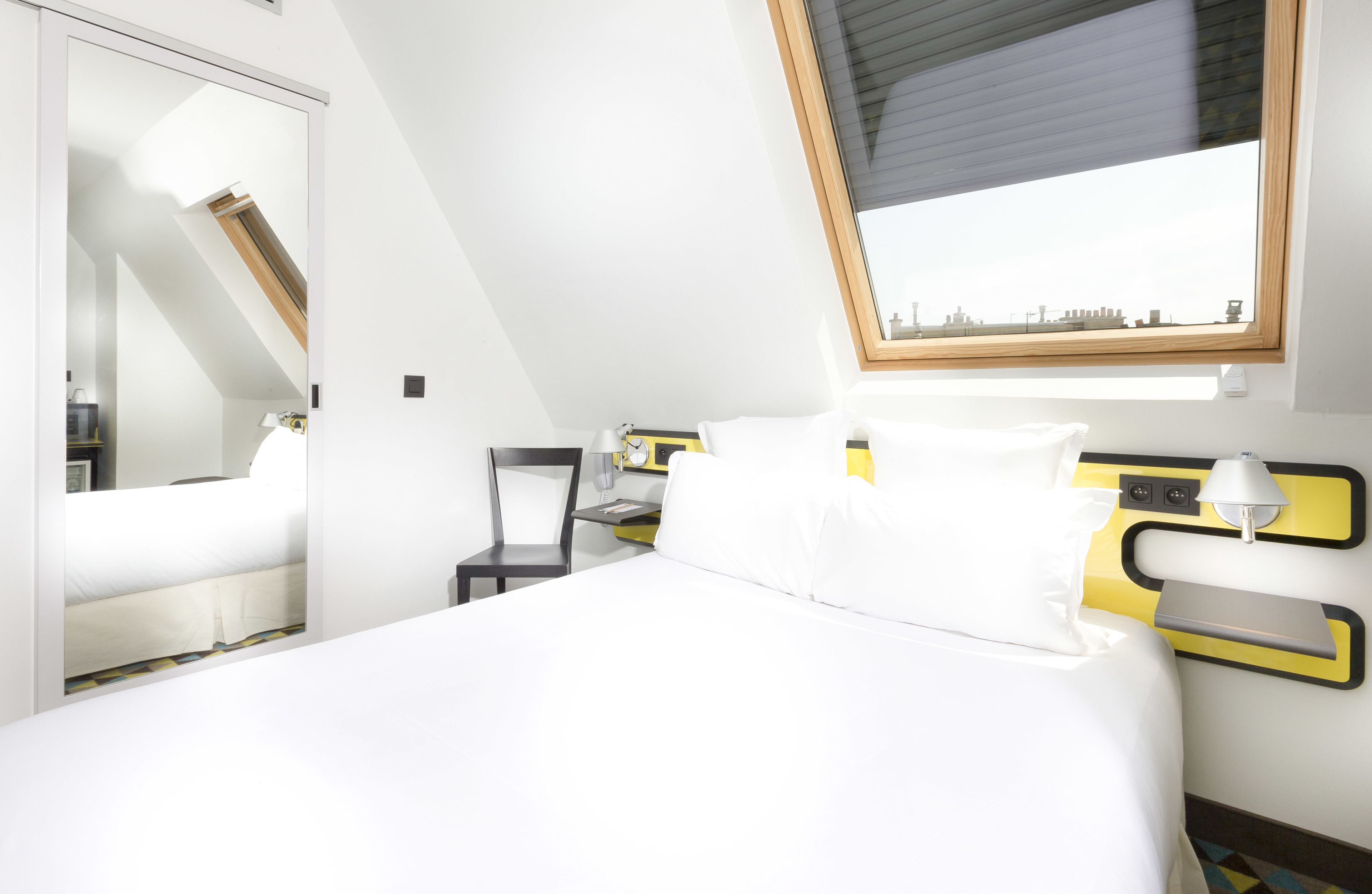 Una habitación de hotel moderna con cama, una silla, un escritorio y ventana con vista a la ciudad.