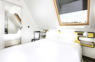 A modern hotel room with a bed, a chair, a desk, and a window with a city view.