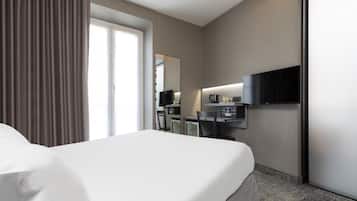 A hotel room with a large bed, a desk with a flat-screen TV, a mirror, and a window with curtains.