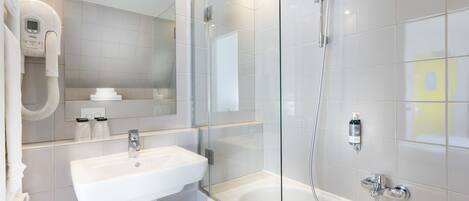 Un baño moderno con lavamanos blanco, ducha con mampara de vidrio y un espejo grande.