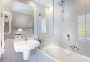 A modern bathroom with a white sink, a glass-enclosed shower, and a large mirror.
