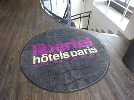 Ένα κυκλικό χαλάκι με την επιγραφή «libertel hotels paris montmartre opera» πάνω σε ένα ξύλινο δάπεδο.