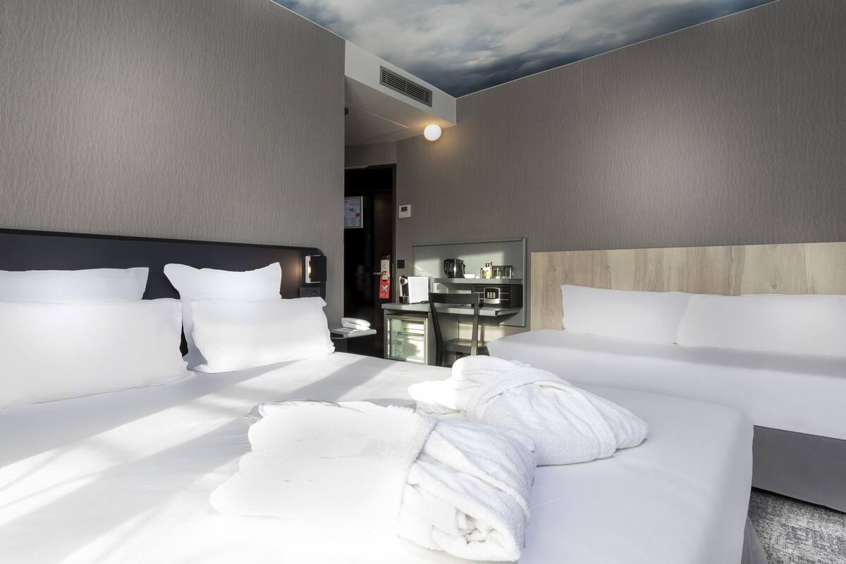 A hotel room with two beds, a minibar, and a ceiling with a cloud design.