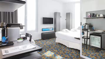 Quarto de hotel com cama, escrivaninha com cafeteira, televisão e minibar.