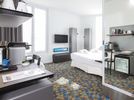 Habitación de hotel con cama, escritorio con cafetera, televisor y minibar.