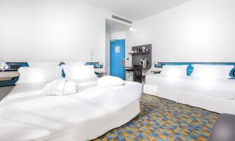 A hotel room with two beds, a small kitchenette, and a bathroom.
