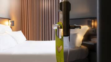 Una habitación de hotel con cama, mesita de noche y panel de control en la pared.