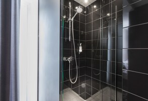 Un bagno moderno con pareti rivestite di piastrelle nere, cabina doccia in vetro e doccetta a vista.