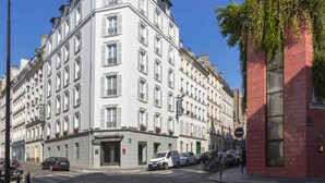 A multi-story hotel with a classic European architectural style, featuring a prominent entrance with a glass door and a balcony with red flowers. - Libertel Montmartre Opéra (Paris)