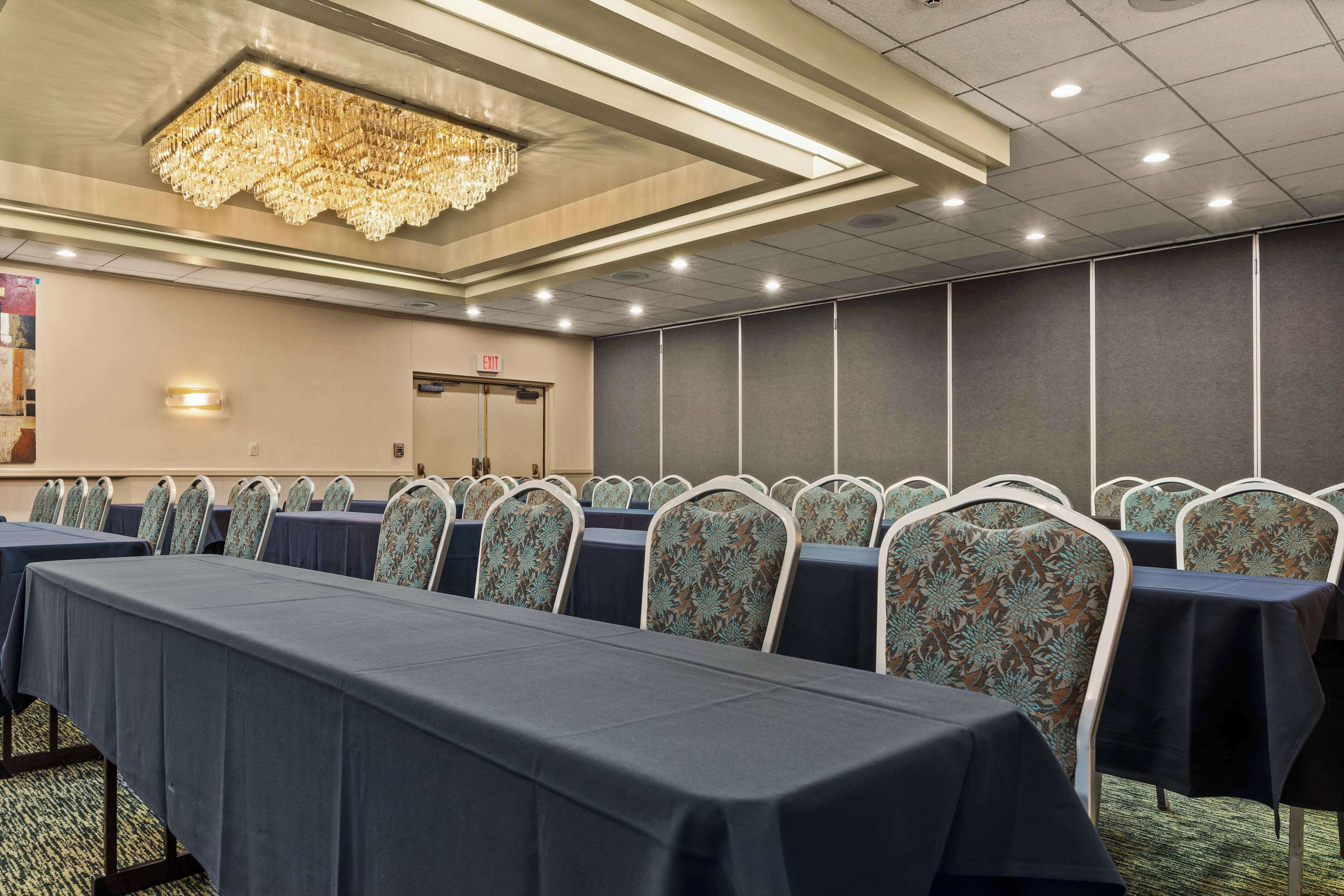 A conference room with rows of tables and chairs, a chandelier, and a door in the background.