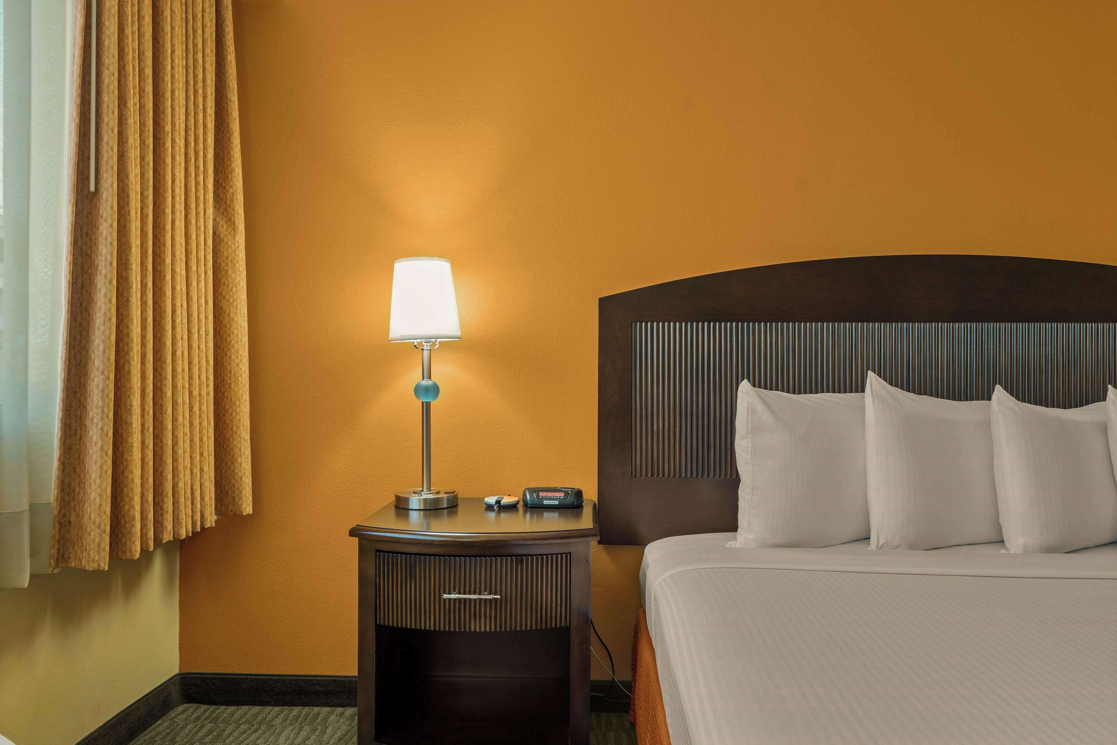 A hotel room with a bed, a nightstand with a lamp, and a wall with a textured panel.