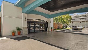 A hotel entrance with a covered walkway, potted plants, and a parking area. - Airport Honolulu Hotel, Trademark Collection by Wyndham (Honolulu)
