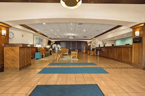 A hotel lobby with a reception desk, seating area, and a large clock on the wall.
