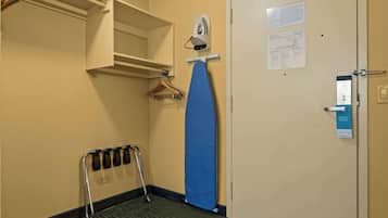 A hotel room with a bed, a wall-mounted ironing board, a hanging rack, and a door with a privacy card.