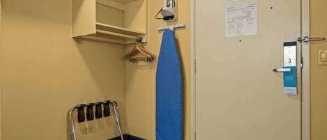 Habitación de hotel con una cama, una plancha de pared, un perchero y una puerta con tarjeta de aviso.