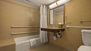 A bathroom with a bathtub, a sink with a mirror, a toilet, and handrails.