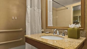 A bathroom with a granite countertop sink, a mirror, a towel dispenser, and a shower curtain.
