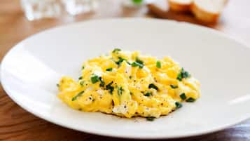 Scrambled eggs on a white plate with chopped herbs on a wooden table.