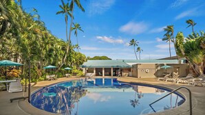 A swimming pool with lounge chairs and umbrellas, surrounded by palm trees and a building with a green roof. - Airport Honolulu Hotel, Trademark Collection by Wyndham (Honolulu)