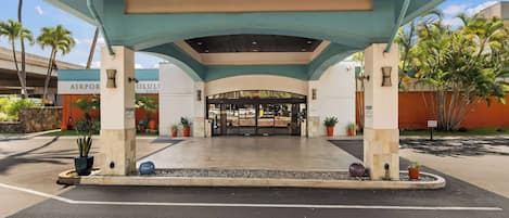 Una entrada cubierta a un hotel con diseño moderno, que presenta un techo plano y un arco central.