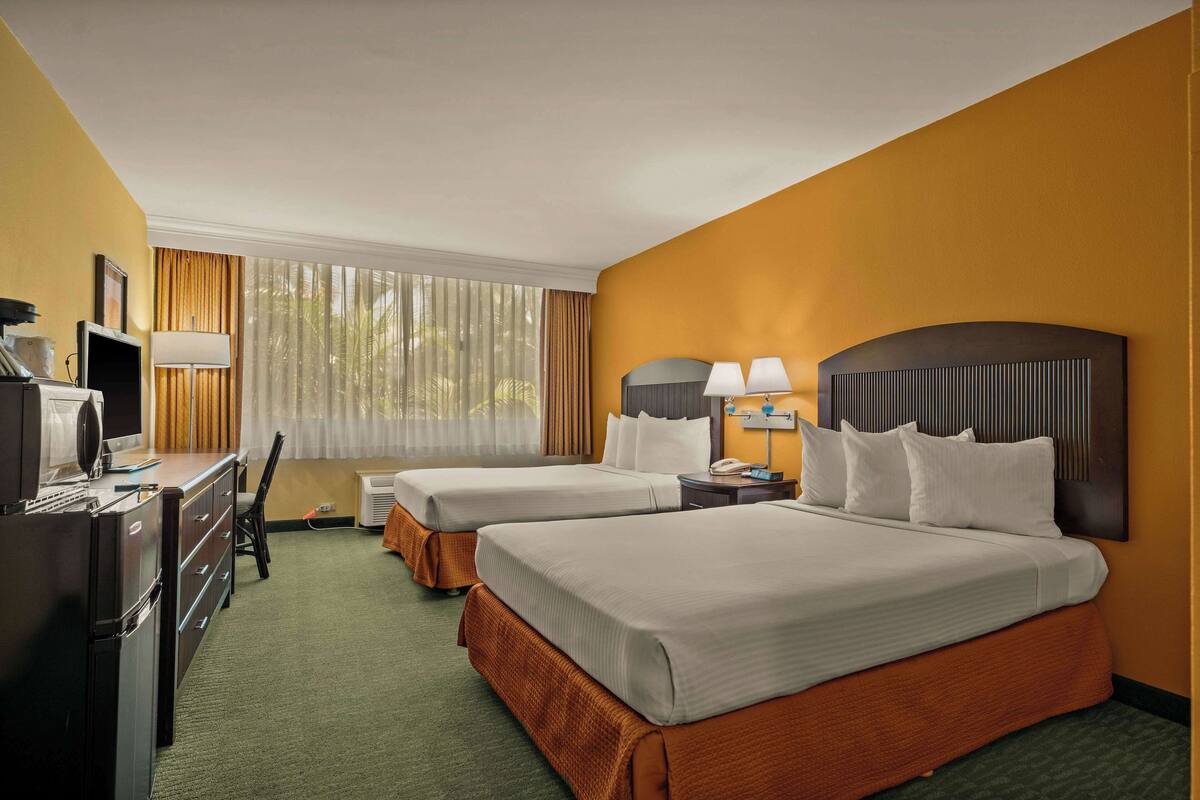 A hotel room with two beds, a desk, a chair, a TV, and a window with curtains.