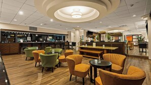 A modern bar area with wooden flooring, green and orange upholstered chairs, and a central bar counter. - Airport Honolulu Hotel, Trademark Collection by Wyndham (Honolulu)