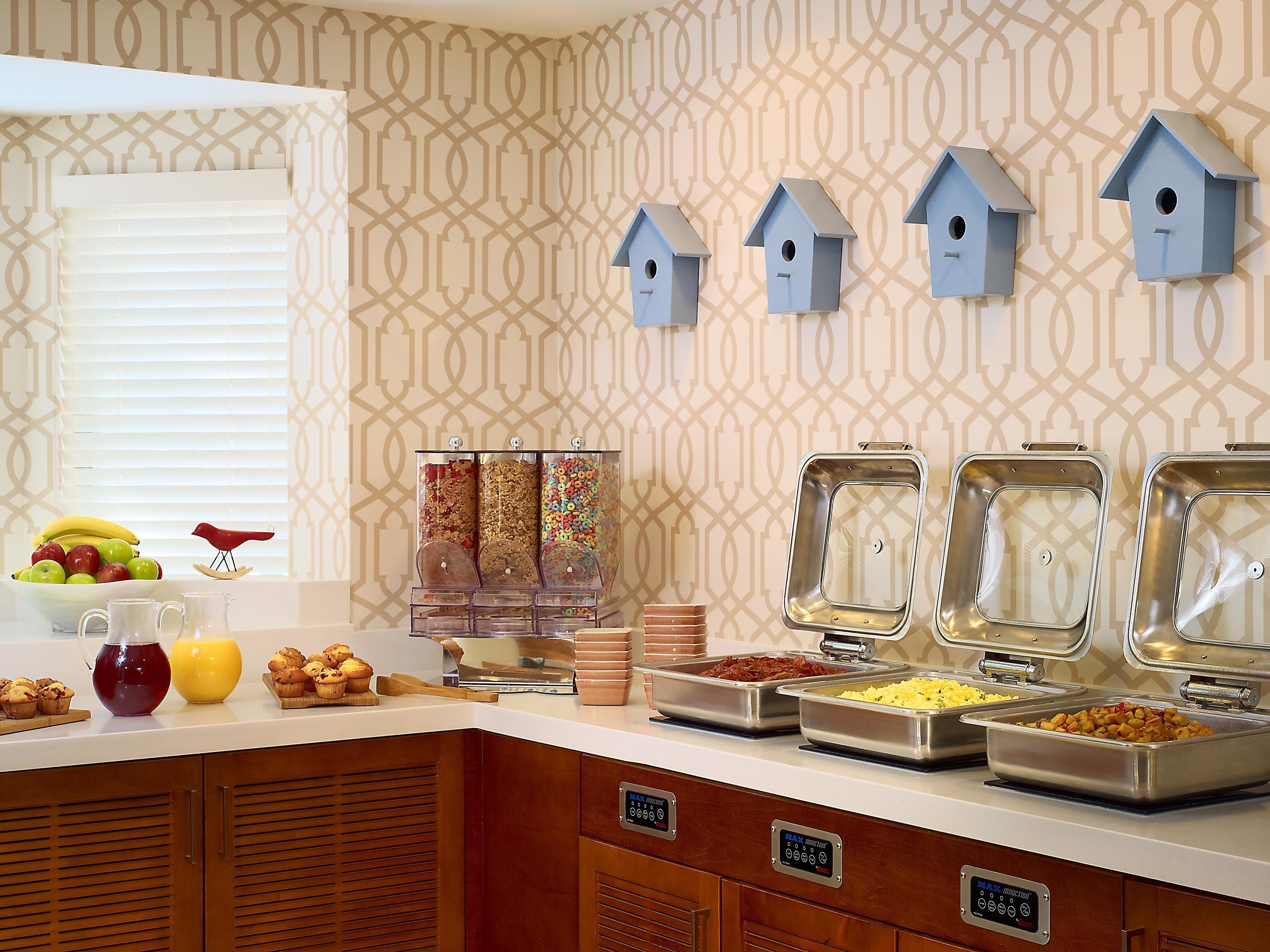 A breakfast buffet with various food items, a fruit bowl, and decorative birdhouses on the wall.