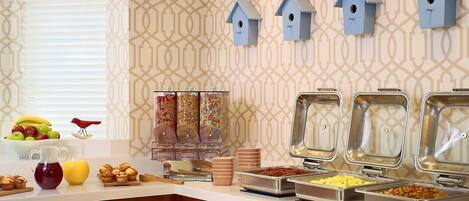 A breakfast buffet with various food items, a fruit bowl, and decorative birdhouses on the wall.