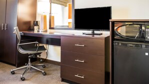 Une chambre d’hôtel équipée d’un bureau, d’une chaise, d’une télévision, d’un four à micro-ondes et d’une armoire.