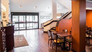 Un hall d’hôtel moderne avec un comptoir d’accueil, un escalier, ainsi que plusieurs tables et chaises pour prendre les repas.