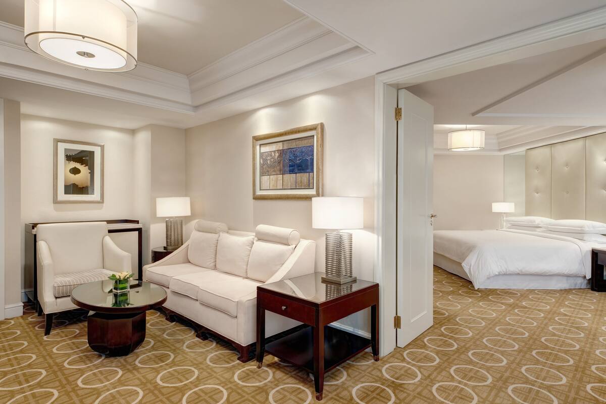 A hotel room with a bed, a sofa, a small table, and a lamp.